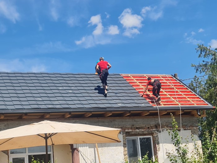 Echipă montând țiglă metalică antracit; jumătate din acoperiș e încă la folie și șipcă